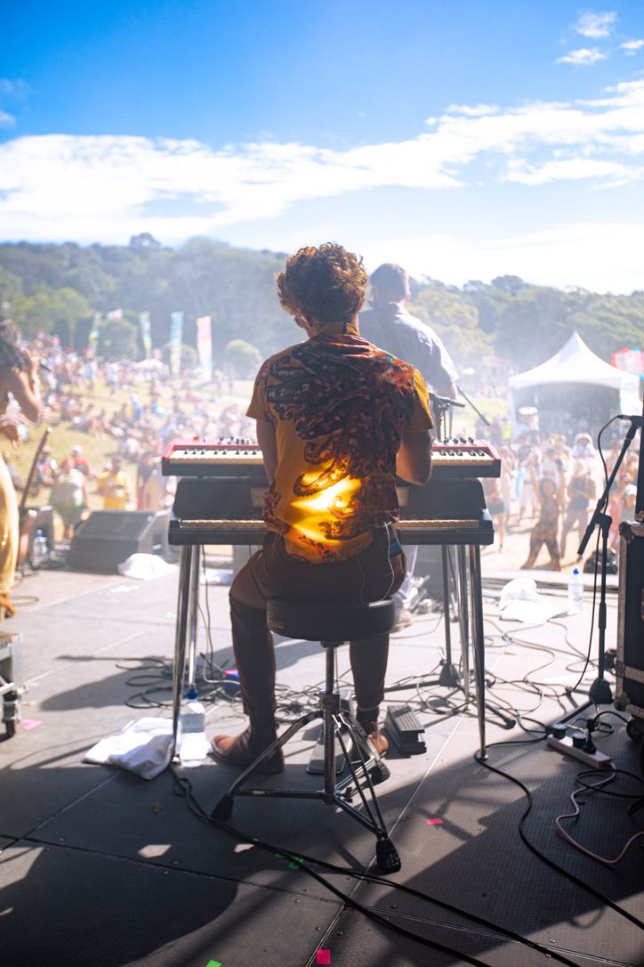 Dillon Rhodes playing two keyboards on stage at Splore Festival, looking out over the sunlit crowd